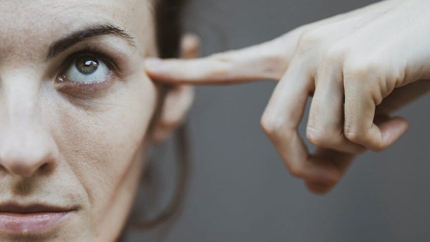 selective focus portrait photo of woman in red t shirt pointing to her head